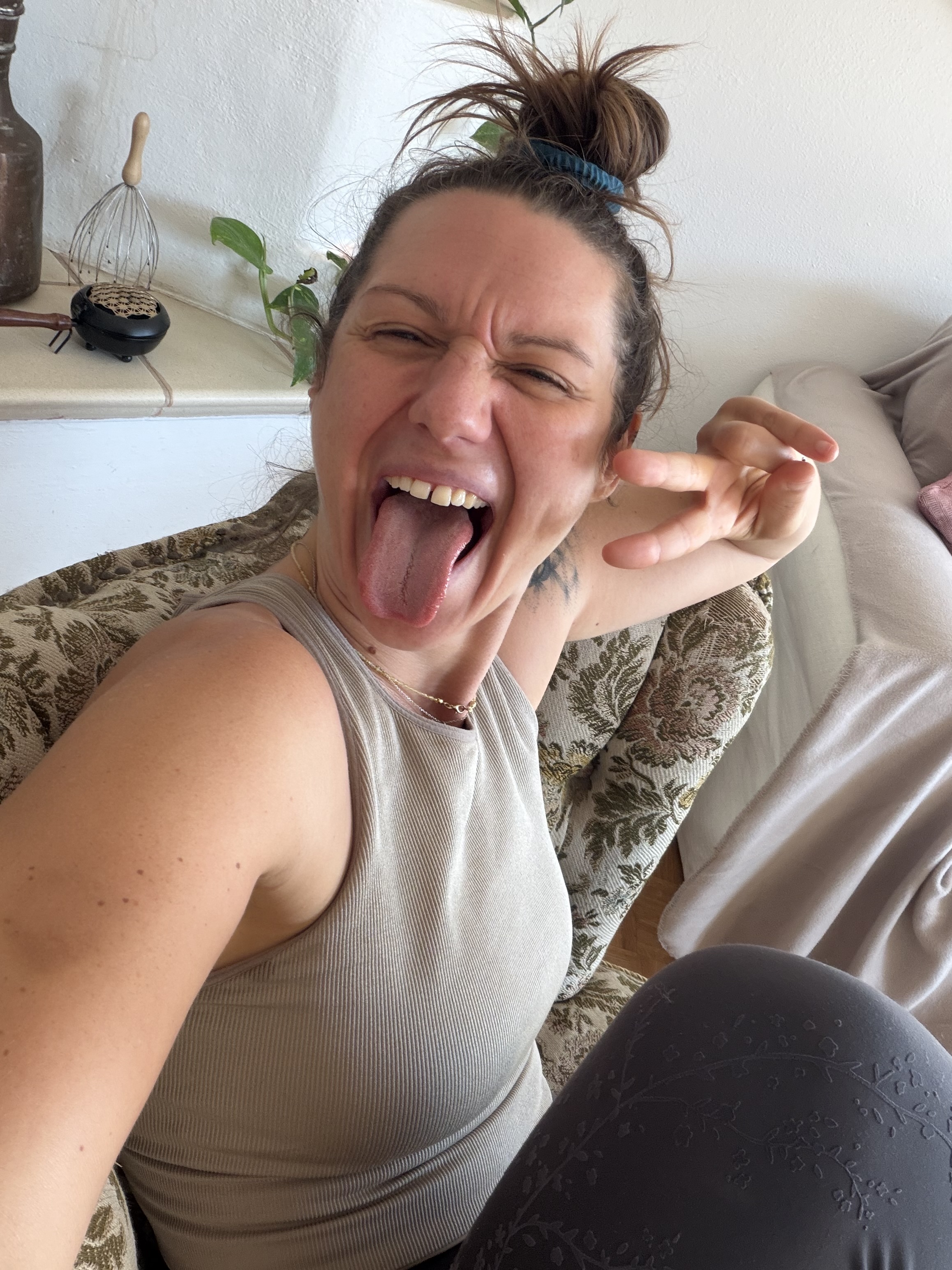 Janina lacht frech auf dem Sofa und zeigt ein Peace-Zeichen